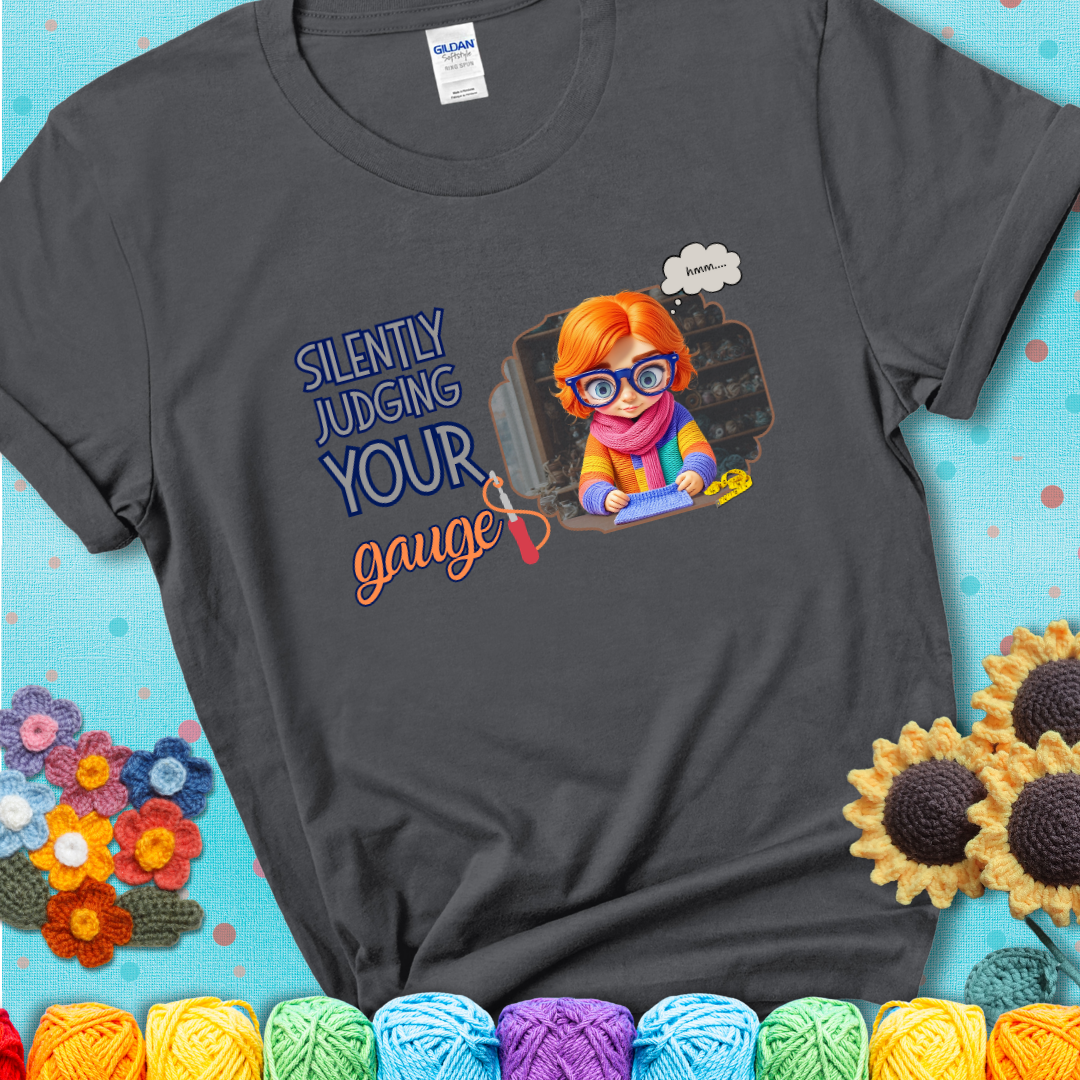 Charcoal t-shirt with a serious-looking crocheter in rainbow clothing and big glasses, holding a tape measure under the phrase “Silently Judging Your Gauge.”