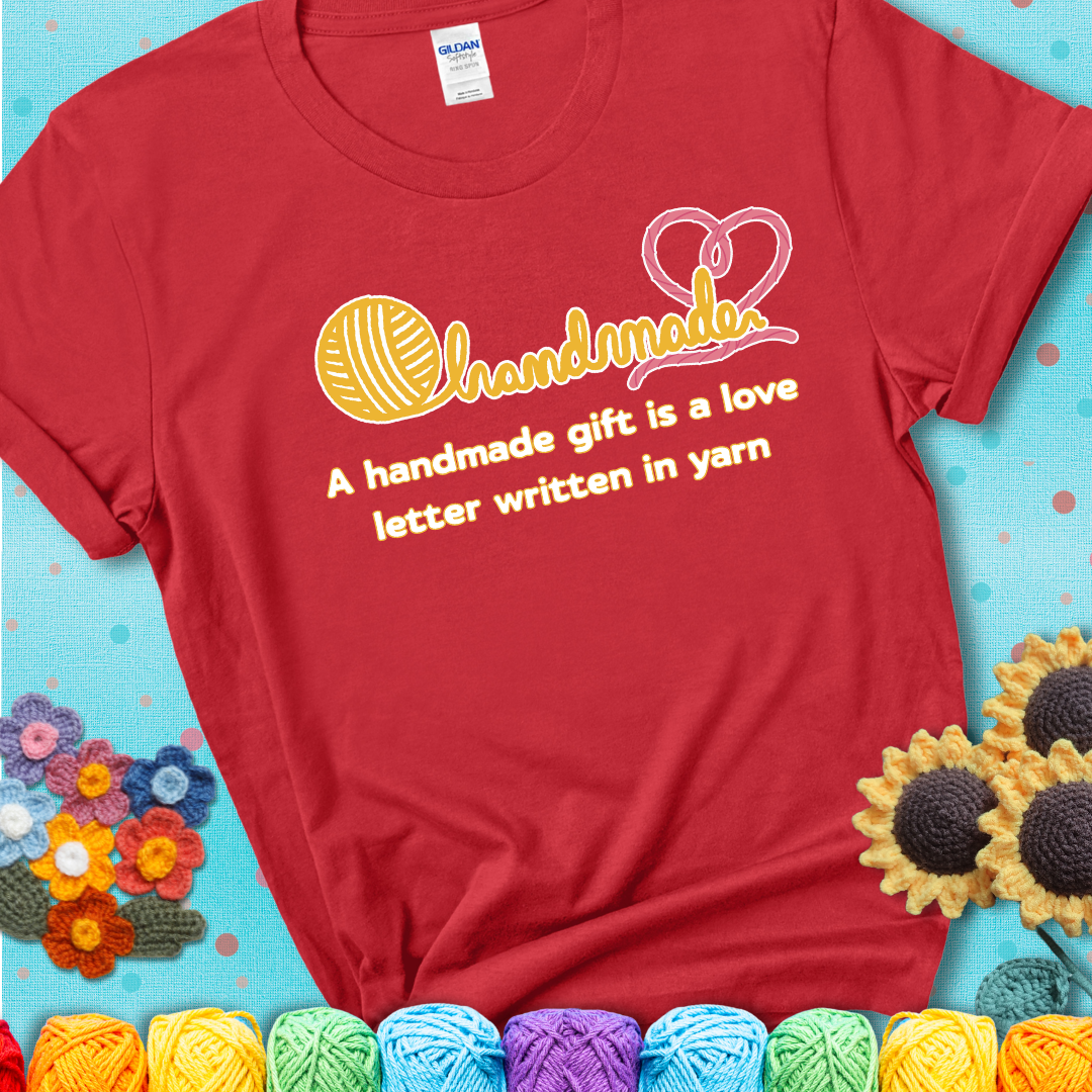 Soft script-style design with heart detail. Text reads: “A Handmade Gift Is a Love Letter Written in Yarn.” A sweet and sentimental shirt for crocheters who craft from the heart, showing a red tee with a teal sunflower background
