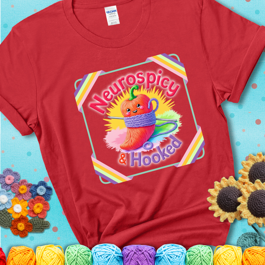 Red t-shirt featuring a smiling red chili pepper wrapped in yarn with a crochet hook, text says “Neurospicy & Hooked.”