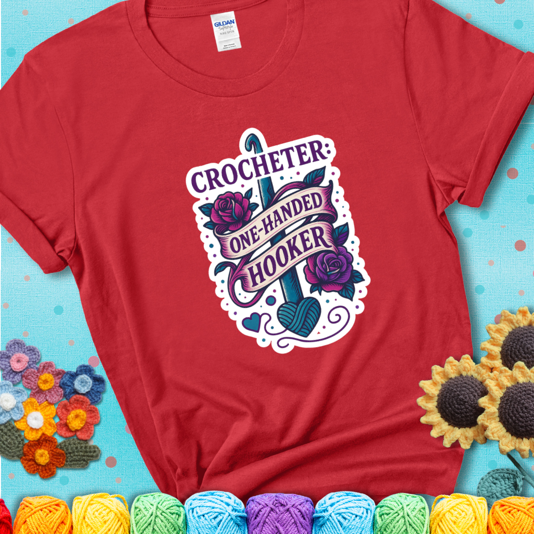 Red t-shirt with a tattoo-style crochet design featuring a crochet hook, roses, and the phrase “Crocheter: One-Handed Hooker.”
