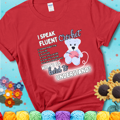 A cute crochet bear holding a yarn ball, surrounded by a short crochet pattern. The phrase reads “I Speak Fluent Crochet – What’s so hard to understand?” on a red t-shirt.