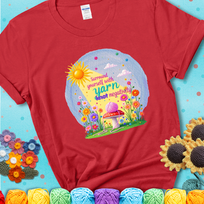 Red t-shirt featuring a happy spring garden scene with a sunbeam, flowers, and a pink yarn ball on a mushroom, with the quote "Surround yourself with yarn, knot negativity."