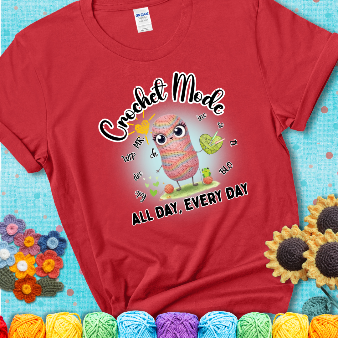 Red t-shirt with a kawaii-style rainbow yarn character surrounded by crochet stitch abbreviations and holding a yarn heart, with text “Crochet Mode All Day, Every Day.”