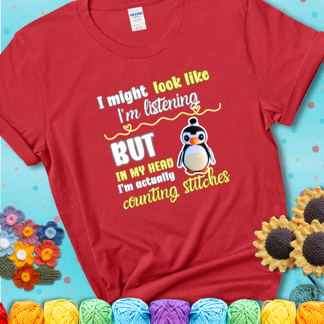Red t-shirt shows a crocheted penguin next to the text “I might look like I’m listening but in my head I’m actually counting stitches.”