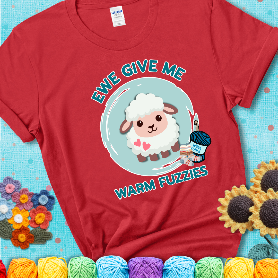 Red t-shirt showing a cartoon sheep with pink hearts, wool socks, and yarn labeled “Wool Classic.” Text reads “Ewe Give Me Warm Fuzzies.”