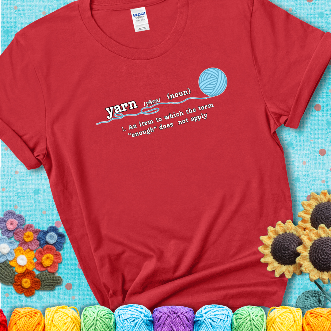 Red t-shirt with a definition-style yarn graphic reading “An item to which the word ‘enough’ does not apply,” plus a blue ball of yarn with a loose strand.