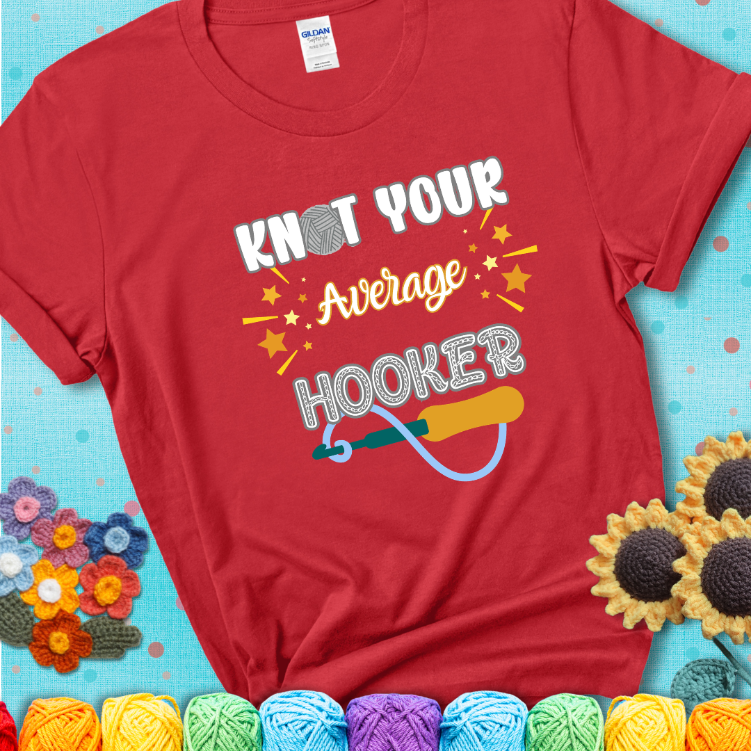 Bold lettering on a red t-shirt with a yarn hook graphic. Text reads: “I'm Not Your Average Hooker.” A cheeky crochet tee for confident crafters who own their skills.