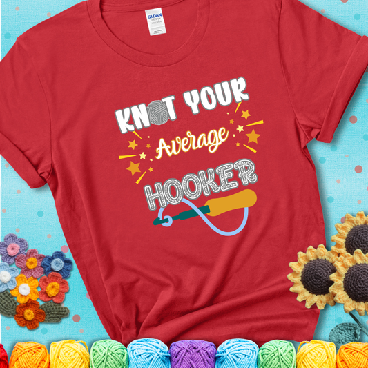 Bold lettering on a red t-shirt with a yarn hook graphic. Text reads: “I'm Not Your Average Hooker.” A cheeky crochet tee for confident crafters who own their skills.
