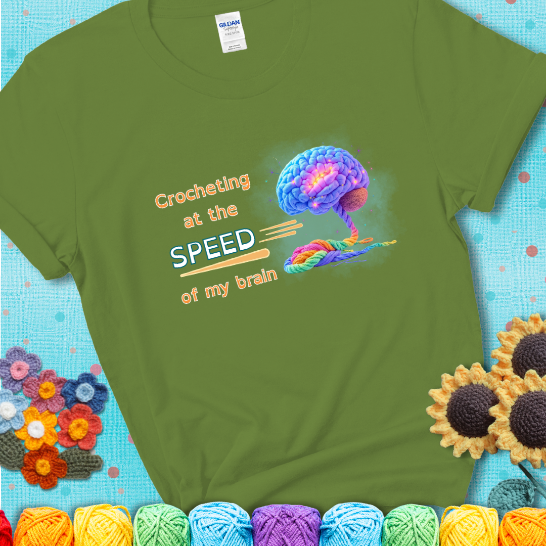 A glowing rainbow brain unravels into colorful yarn with the phrase “Crocheting at the speed of my brain” on a green t-shirt. 