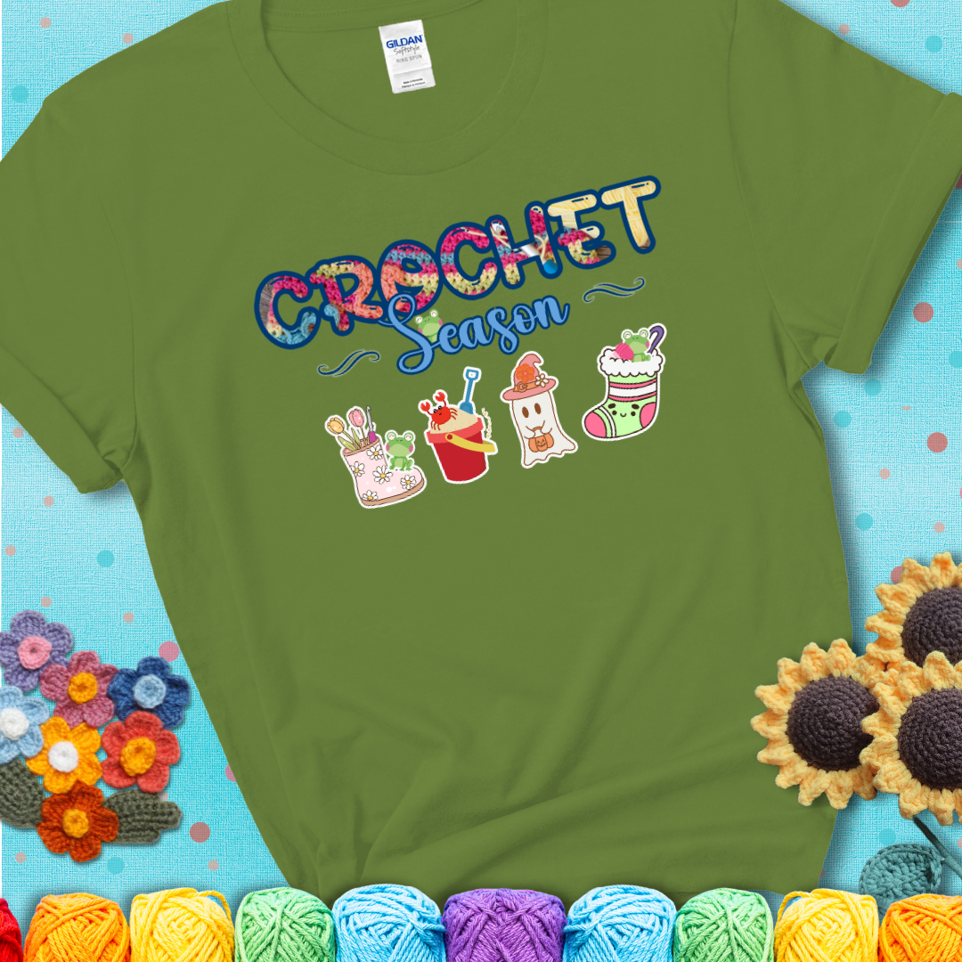 Green t-shirt shows the words “Crochet Season” with cute seasonal icons below: a spring boot with hooks, summer bucket with crab, fall ghost with pumpkin hat, and winter stocking, with tiny frogs.