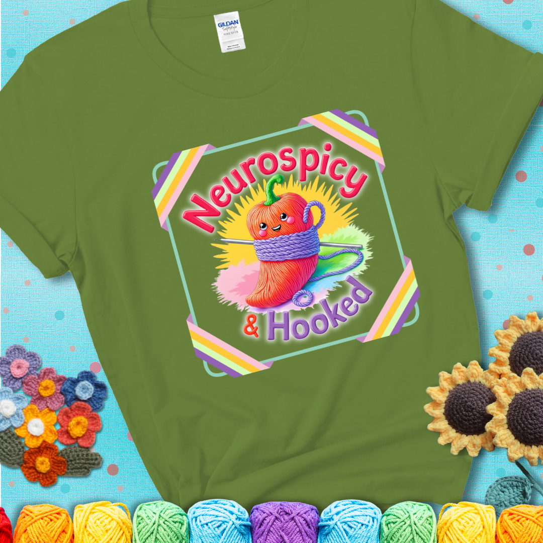 Green t-shirt featuring a smiling red chili pepper wrapped in yarn with a crochet hook, text says “Neurospicy & Hooked.”