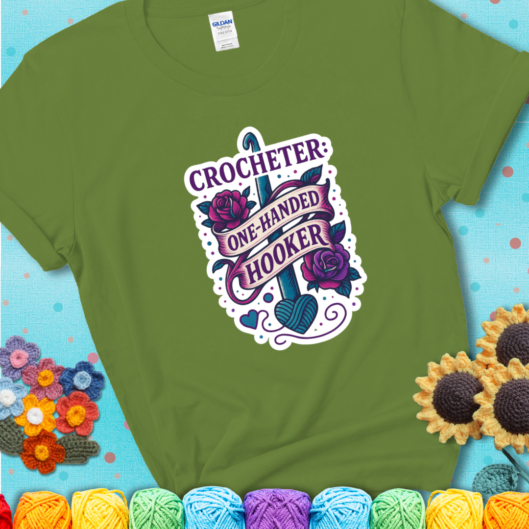Kiwi t-shirt with a tattoo-style crochet design featuring a crochet hook, roses, and the phrase “Crocheter: One-Handed Hooker.”