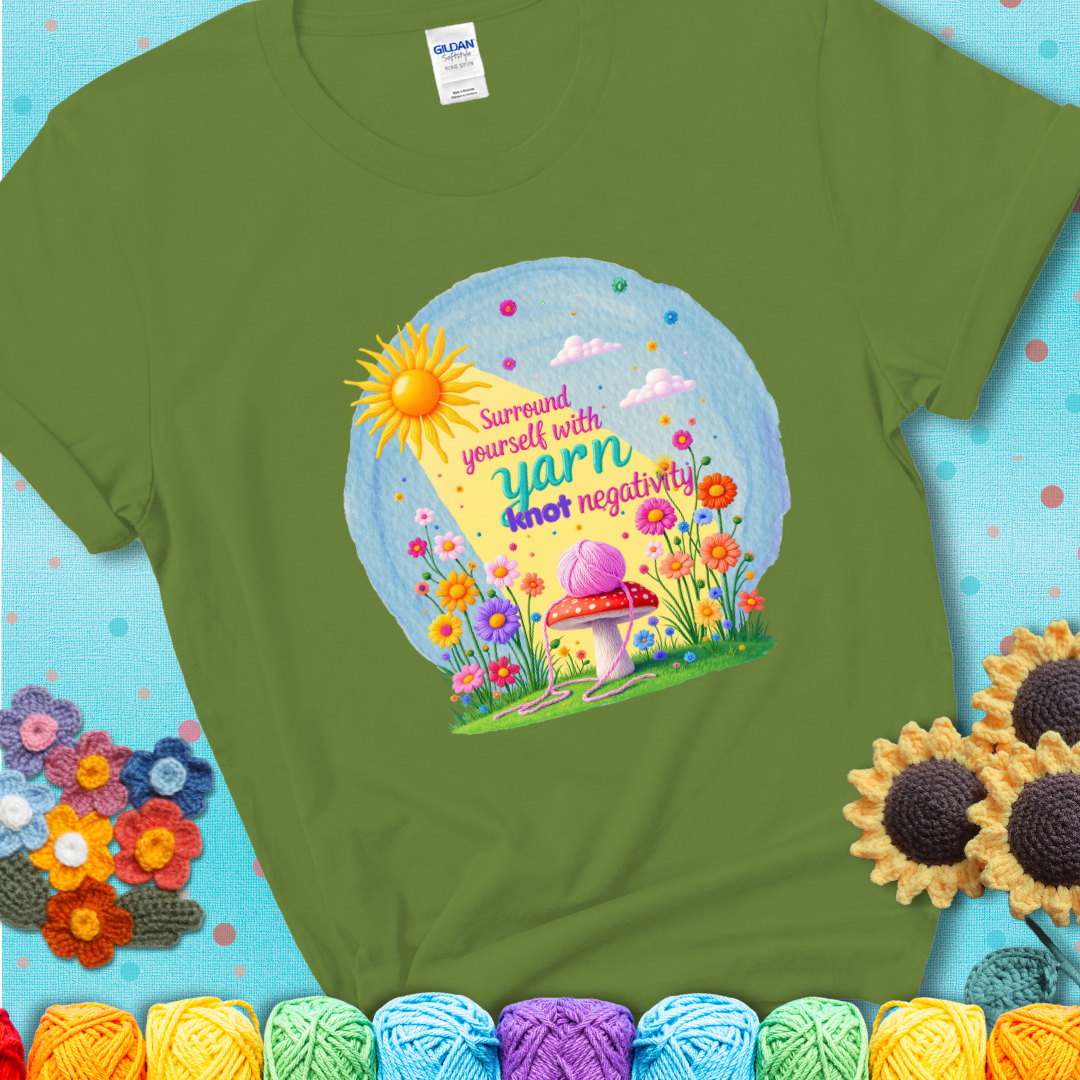 Green t-shirt featuring a happy spring garden scene with a sunbeam, flowers, and a pink yarn ball on a mushroom, with the quote "Surround yourself with yarn, knot negativity."