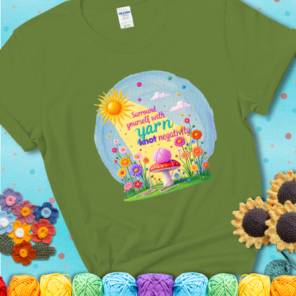 Green t-shirt featuring a happy spring garden scene with a sunbeam, flowers, and a pink yarn ball on a mushroom, with the quote "Surround yourself with yarn, knot negativity."