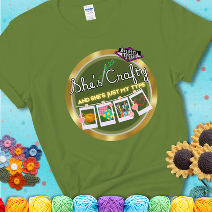 Text on green tee reads "She’s Crafty & She’s Just My Type" with yarn, fabric, painting, and cross-stitch icons hanging like Polaroids