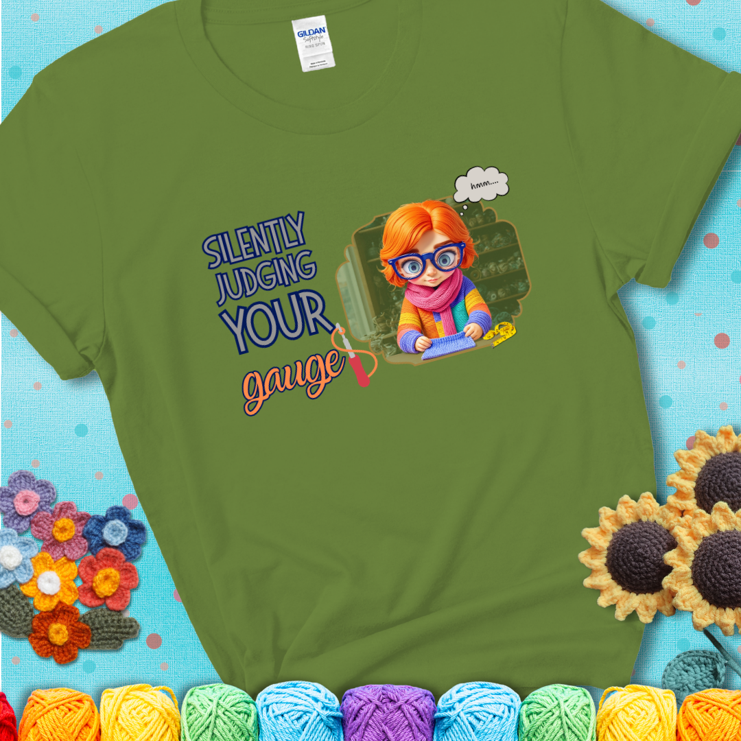 Kiwi t-shirt with a serious-looking crocheter in rainbow clothing and big glasses, holding a tape measure under the phrase “Silently Judging Your Gauge.”