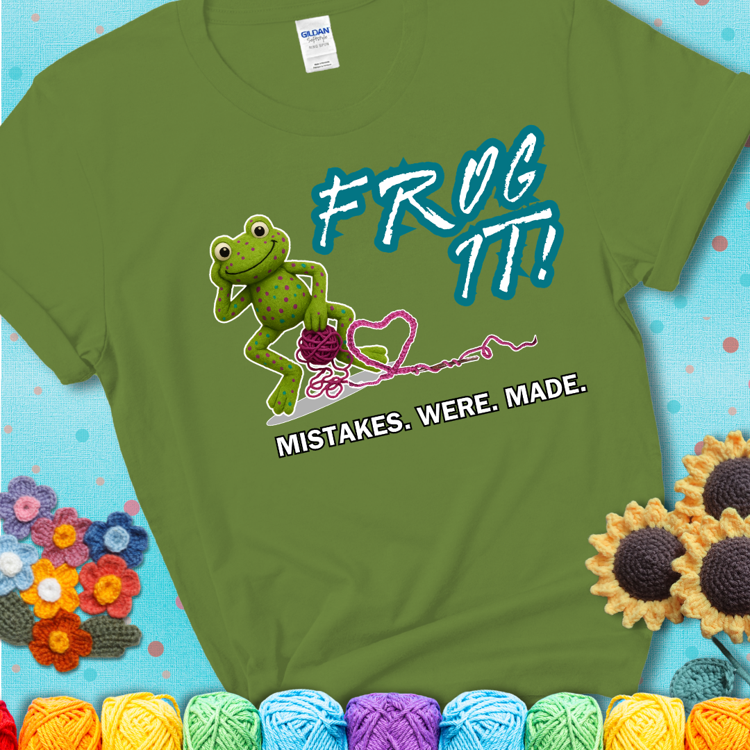 Green frog with yarn and heart-shaped loop. Text reads: “Frog It! Mistakes Were Made.” A playful crochet tee for anyone who's ever had to rip it back, showing a green tee with a teal sunflower background