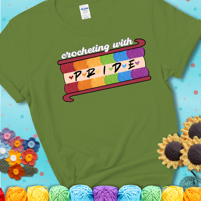 Yarn skeins in rainbow colors stacked in a hook shape. Text reads “Crocheting With Pride” showing a green tee with a teal sunflower background