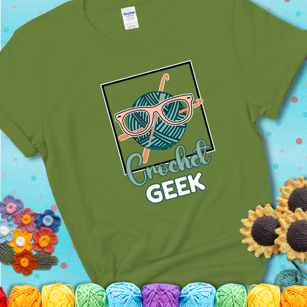 A teal yarn ball with crisscrossed hooks wears oversized nerdy glasses with the phrase “Crochet Geek” in bold, fun text below on a green t-shirt.