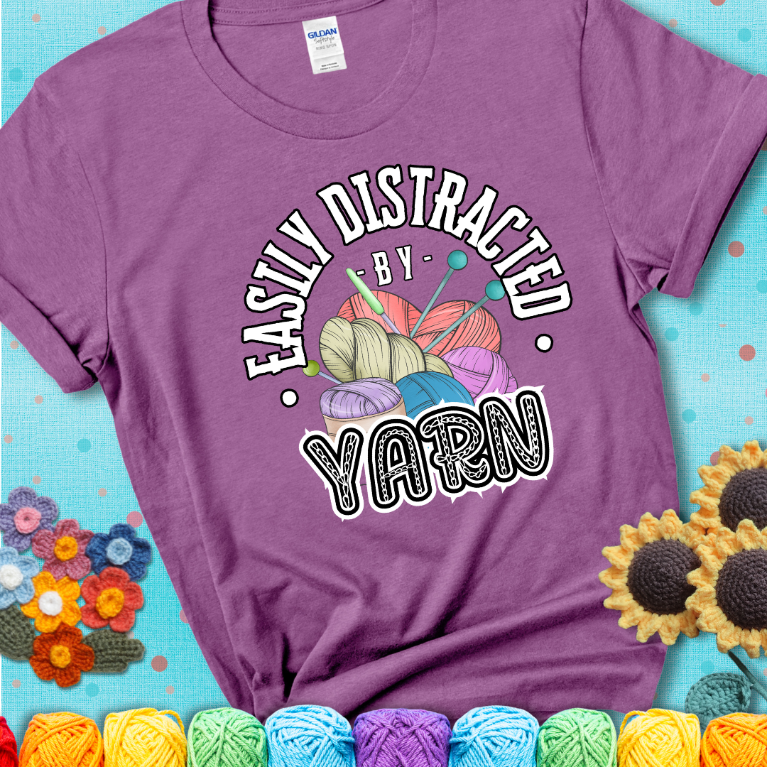 If yarn steals your focus every Design reads 'Easily Distracted By Yarn', perfect crochet gift for yarn lovers; showing a lavender tee with a teal sunflower background