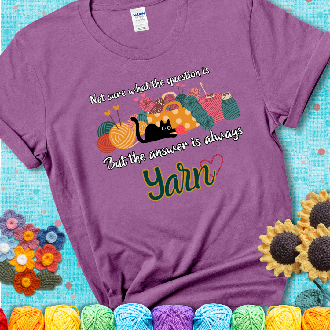 Heather radiant orchid t-shirt with a black cat beside a basket of colorful yarn and the phrase, “Not Sure What The Question Was, But The Answer Is Yarn.”