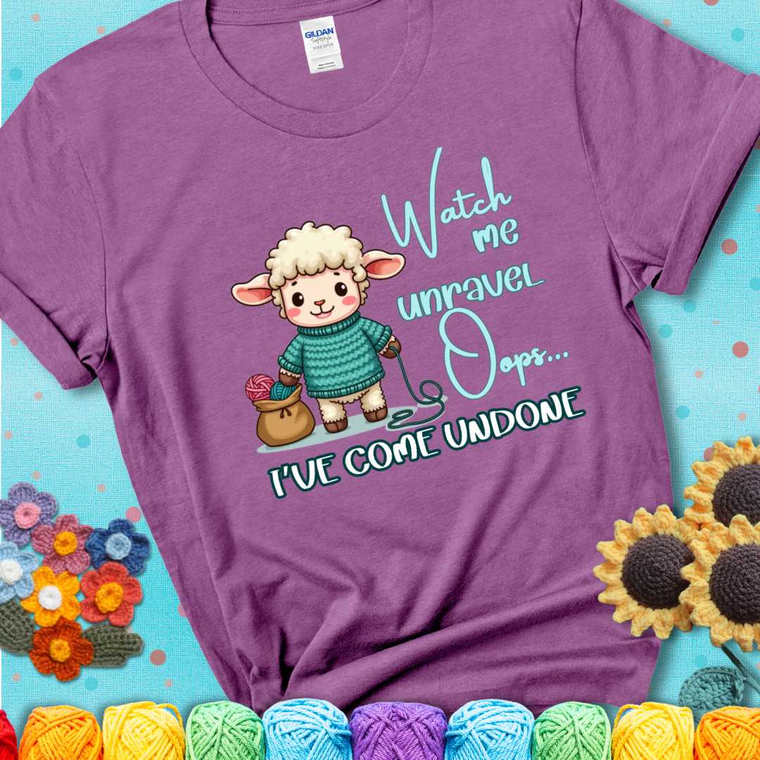 Light purple t-shirt with a cute sheep holding yarn looks startled with the phrase “Watch me unravel… Oops, I’ve come undone.” Perfect mix of whimsy and yarn life chaos.