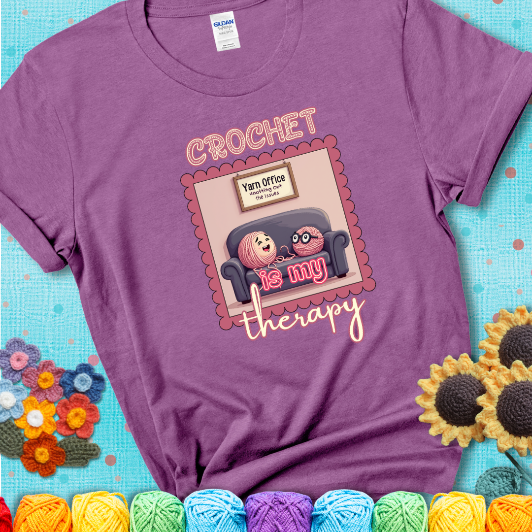 Light purple t-shirt showing a simple text design with yarn cartoon figures. Text reads: “Crochet is My Therapy.” A calming tee for fiber lovers who find healing in every stitch.