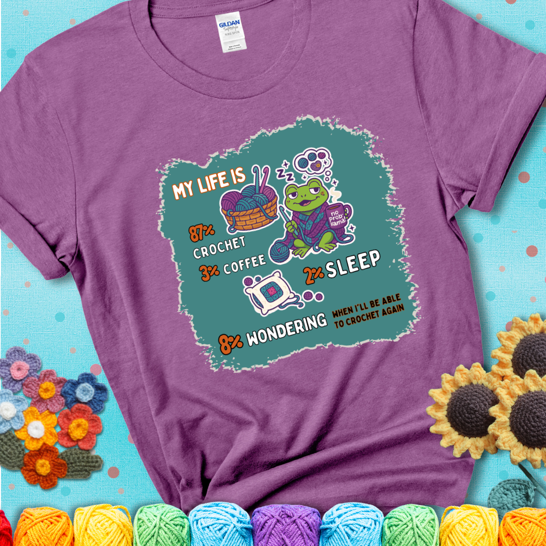 Heather Radiant Orchid t-shirt with a crocheting frog, coffee, yarn, and text showing a playful life breakdown: 87% crochet, 3% coffee, 2% sleep, 8% wondering when to crochet again.
