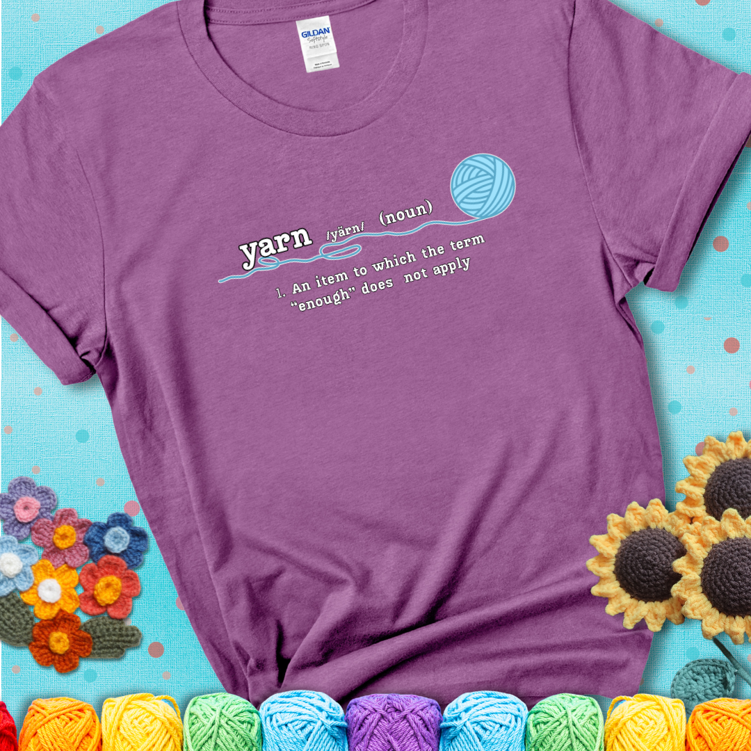 Heather Radiant Orchid t-shirt with a definition-style yarn graphic reading “An item to which the word ‘enough’ does not apply,” plus a blue ball of yarn with a loose strand.