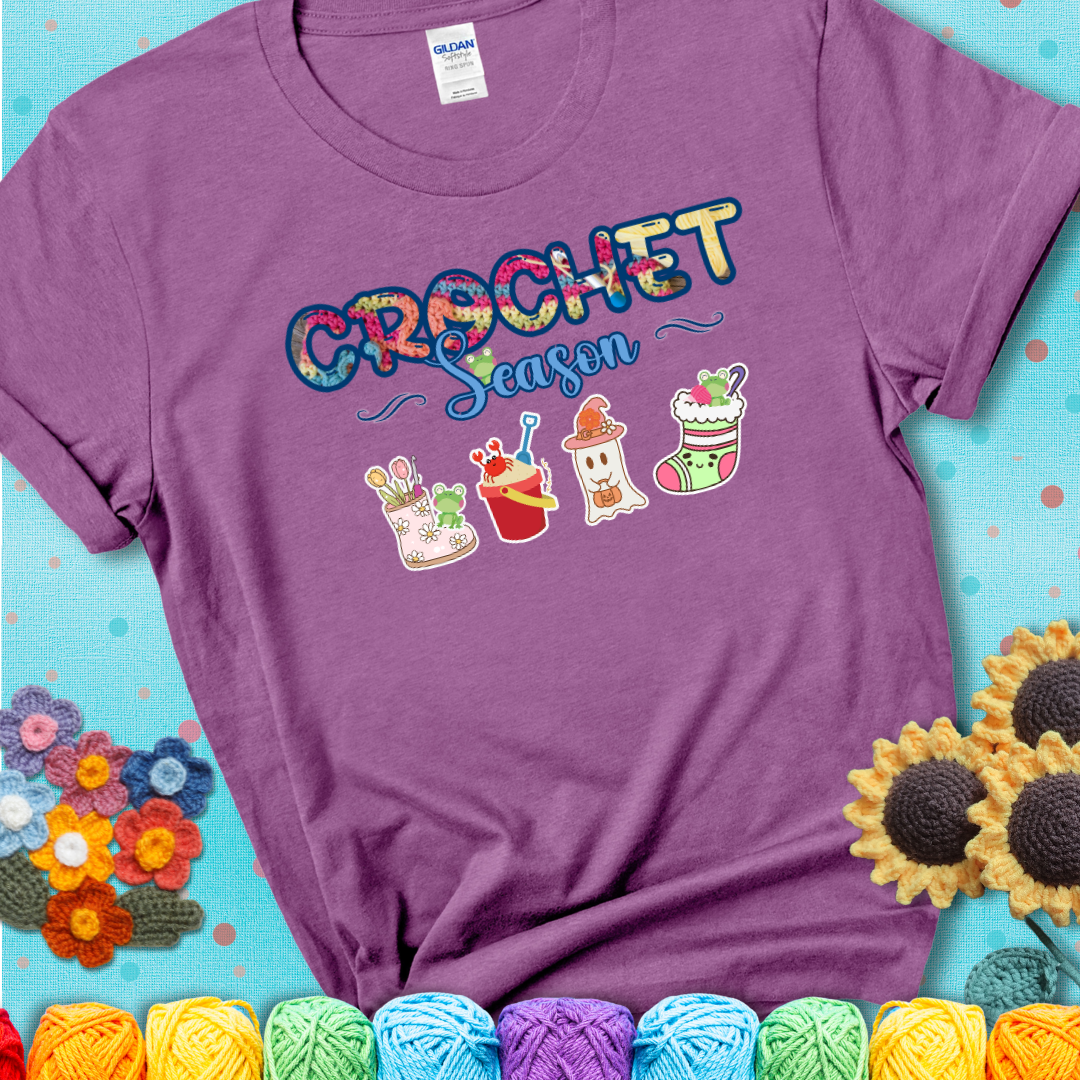Light purple t-shirt shows the words “Crochet Season” with cute seasonal icons below: a spring boot with hooks, summer bucket with crab, fall ghost with pumpkin hat, winter stocking, and tiny frogs.