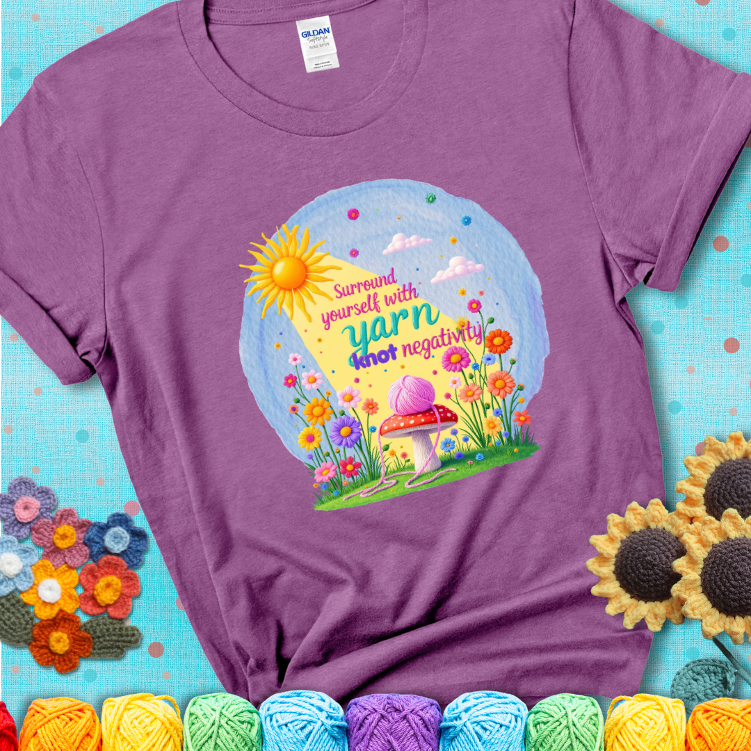 Light purple t-shirt featuring a happy spring garden scene with a sunbeam, flowers, and a pink yarn ball on a mushroom, with the quote "Surround yourself with yarn, knot negativity."