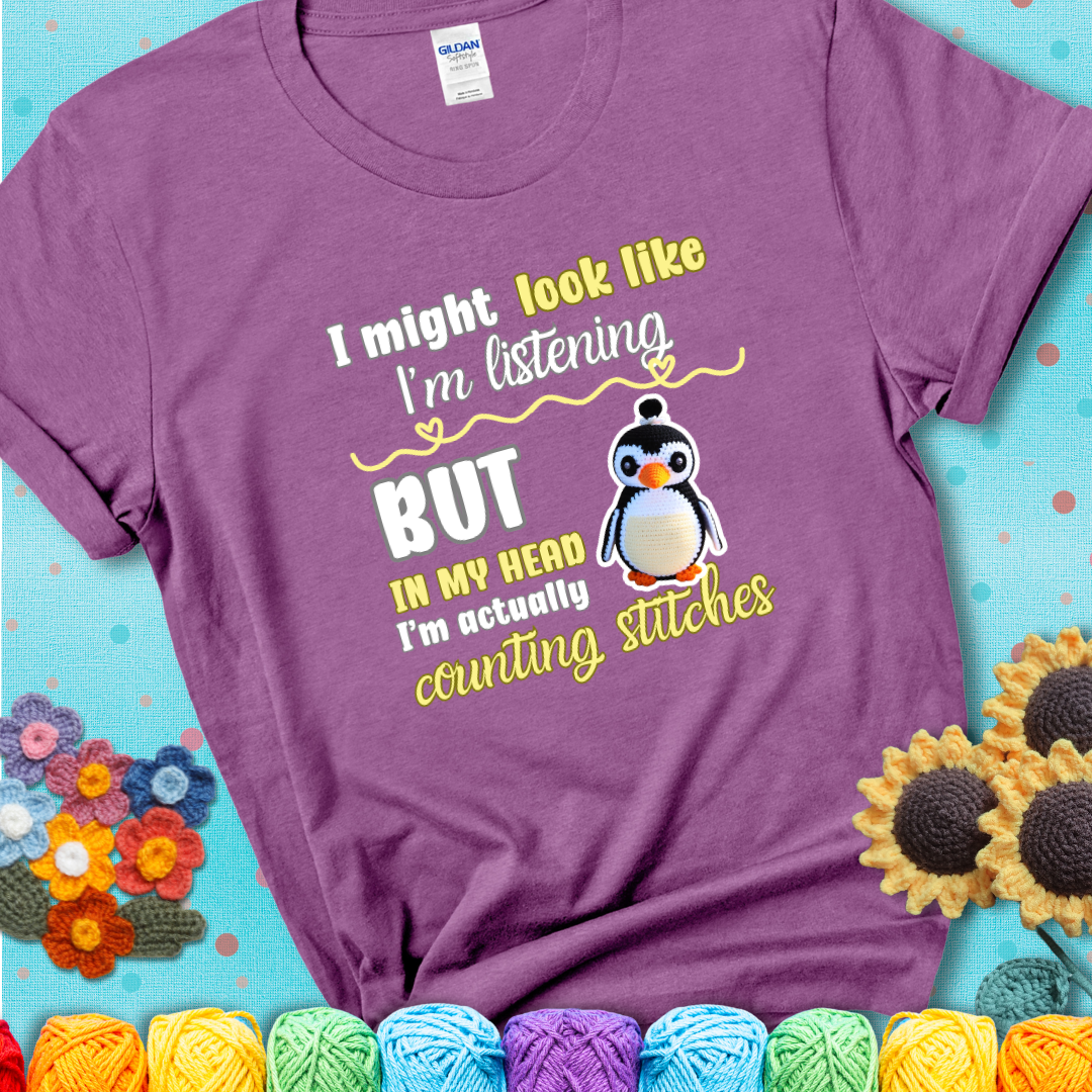 Light purple t-shirt shows a crocheted penguin next to the text “I might look like I’m listening but in my head I’m actually counting stitches.”