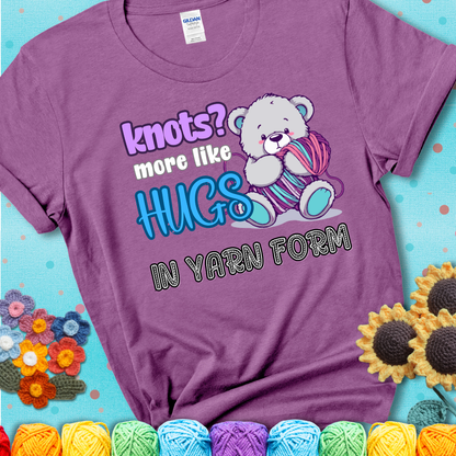 Cute teddy bear holding colorful yarn ball with hearts. Text reads: “Knots? More Like Hugs in Yarn Form.” Perfect for cozy gift-givers and yarn lovers, showing a lavender tee with a teal sunflower background