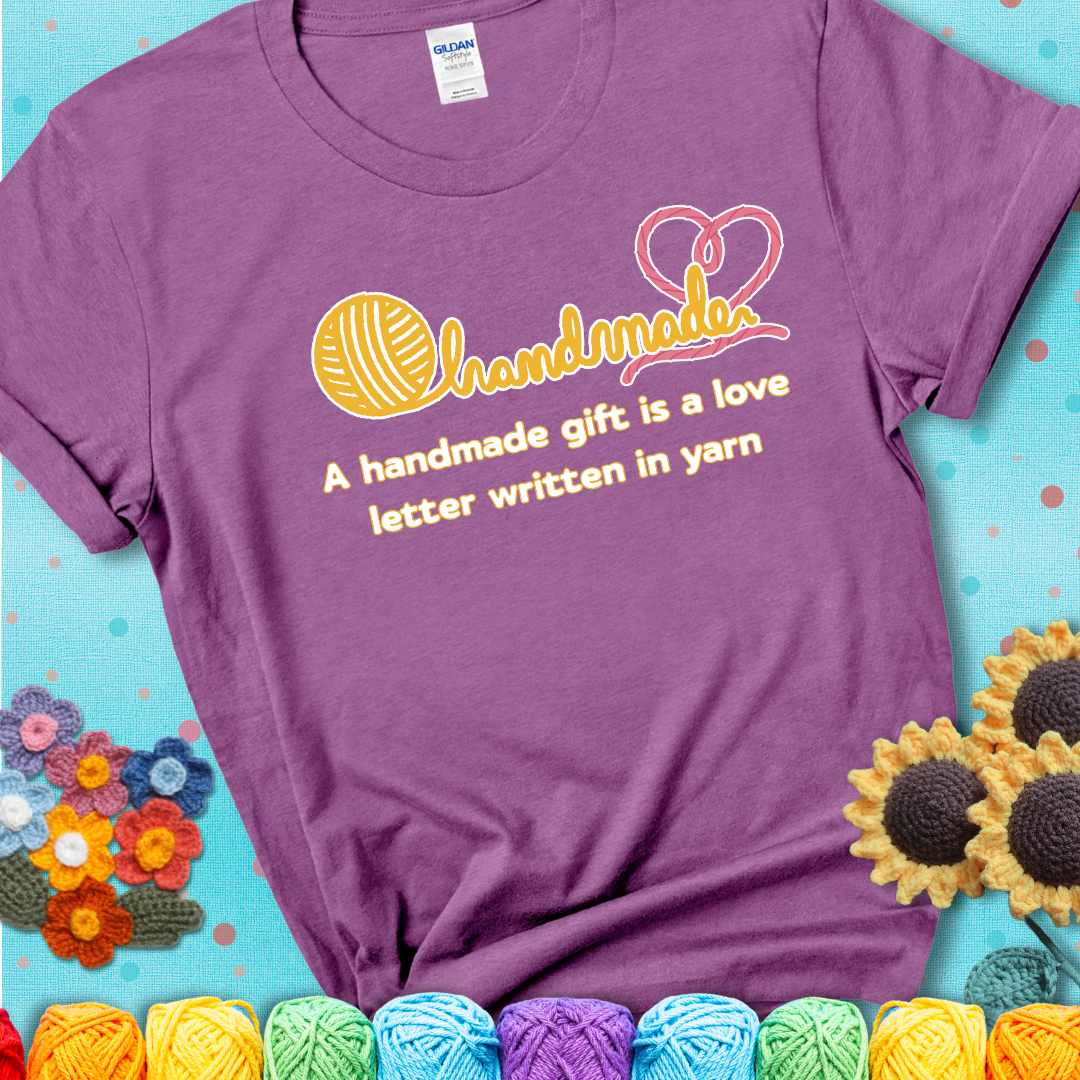 Soft script-style design with heart detail. Text reads: “A Handmade Gift Is a Love Letter Written in Yarn.” A sweet and sentimental shirt for crocheters who craft from the heart, showing a lavender tee with a teal sunflower background
