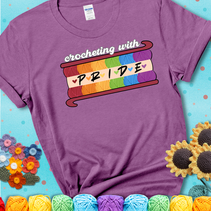 Yarn skeins in rainbow colors stacked in a hook shape. Text reads “Crocheting With Pride” showing a lavender tee with a teal sunflower background