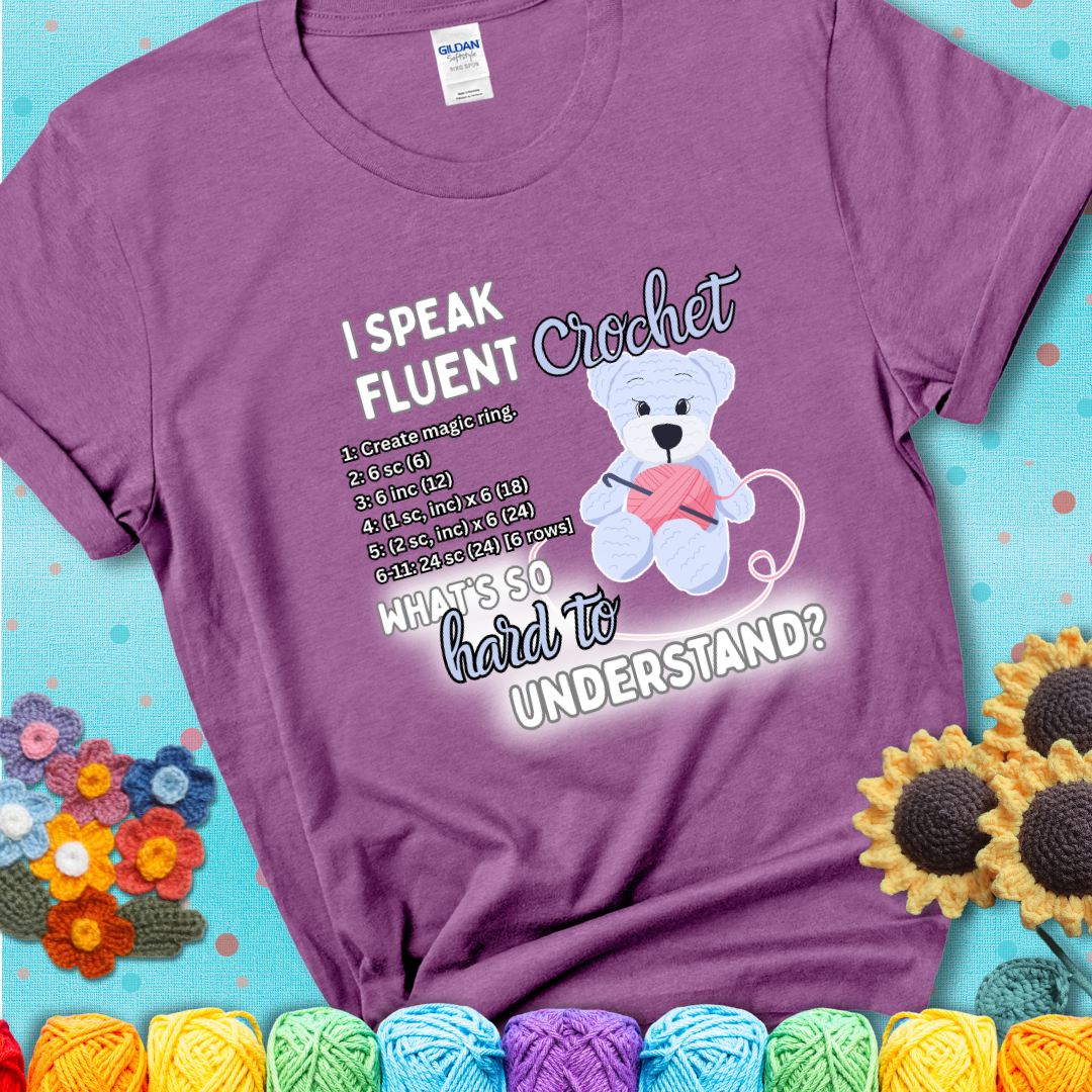 A cute crochet bear holding a yarn ball, surrounded by a short crochet pattern. The phrase reads “I Speak Fluent Crochet – What’s so hard to understand?” on a light purple t-shirt.