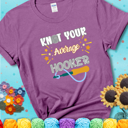 Bold lettering on a light purple t-shirt with a yarn hook graphic. Text reads: “I'm Not Your Average Hooker.” A cheeky crochet tee for confident crafters who own their skills.