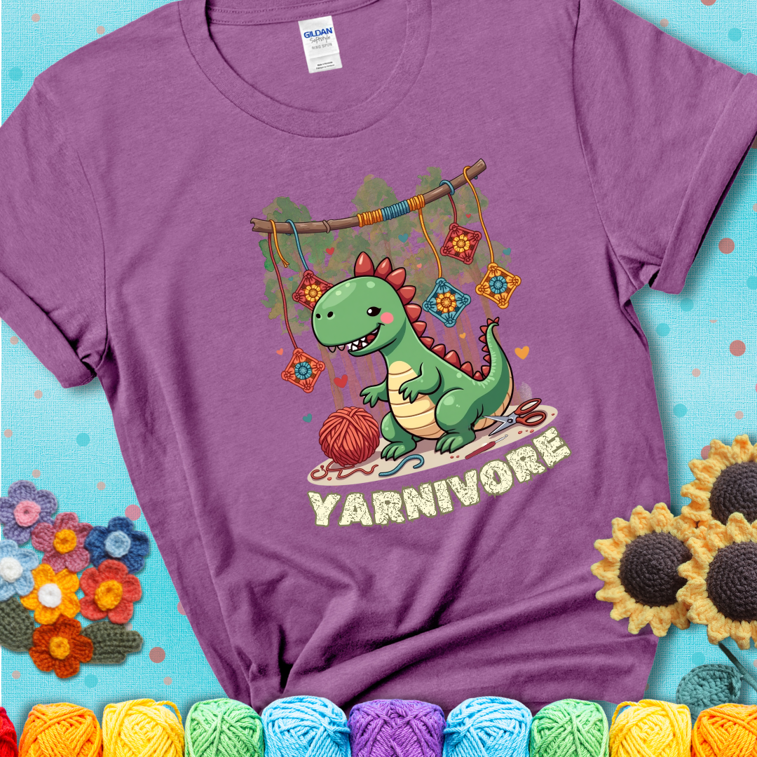 Light purple t-shirt shows a cute green dinosaur with yarn ball and granny squares, text “Yarnivore”, a fun crochet shirt for dino and yarn fans.