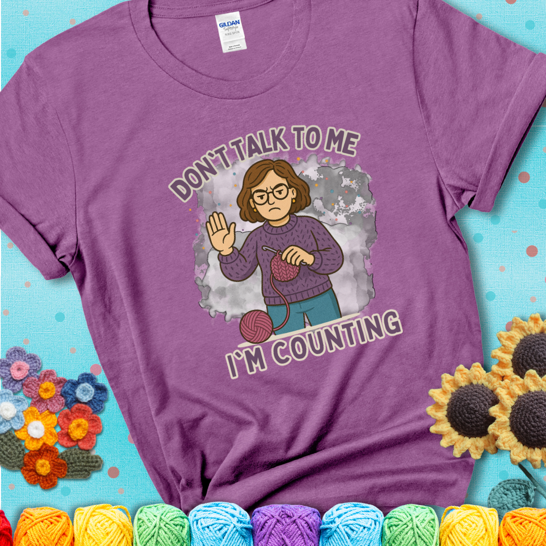 Heather Radiant Orchid t-shirt with an annoyed maker holding up a hand beside yarn, with the phrase “Don’t Talk To Me, I’m Counting.”