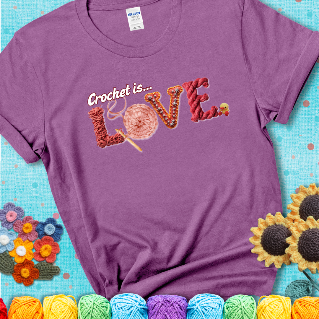 A light purple t-shirt featuring the word "LOVE" spelled with different crochet textures and yarn in red tones, with the phrase “Crochet is…” above in script.