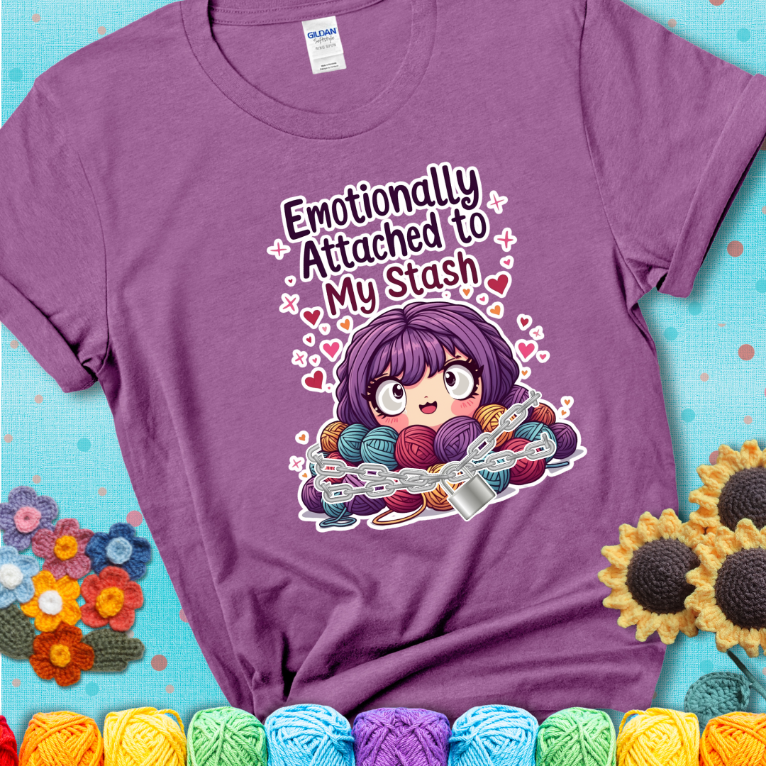 Adorable character with wide eyes hugging a yarn stash wrapped in chains and a lock, with the text “Emotionally Attached to My Stash”  on a lavender tee.