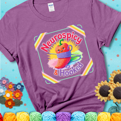 Light purple t-shirt featuring a smiling red chili pepper wrapped in yarn with a crochet hook, text says “Neurospicy & Hooked.”