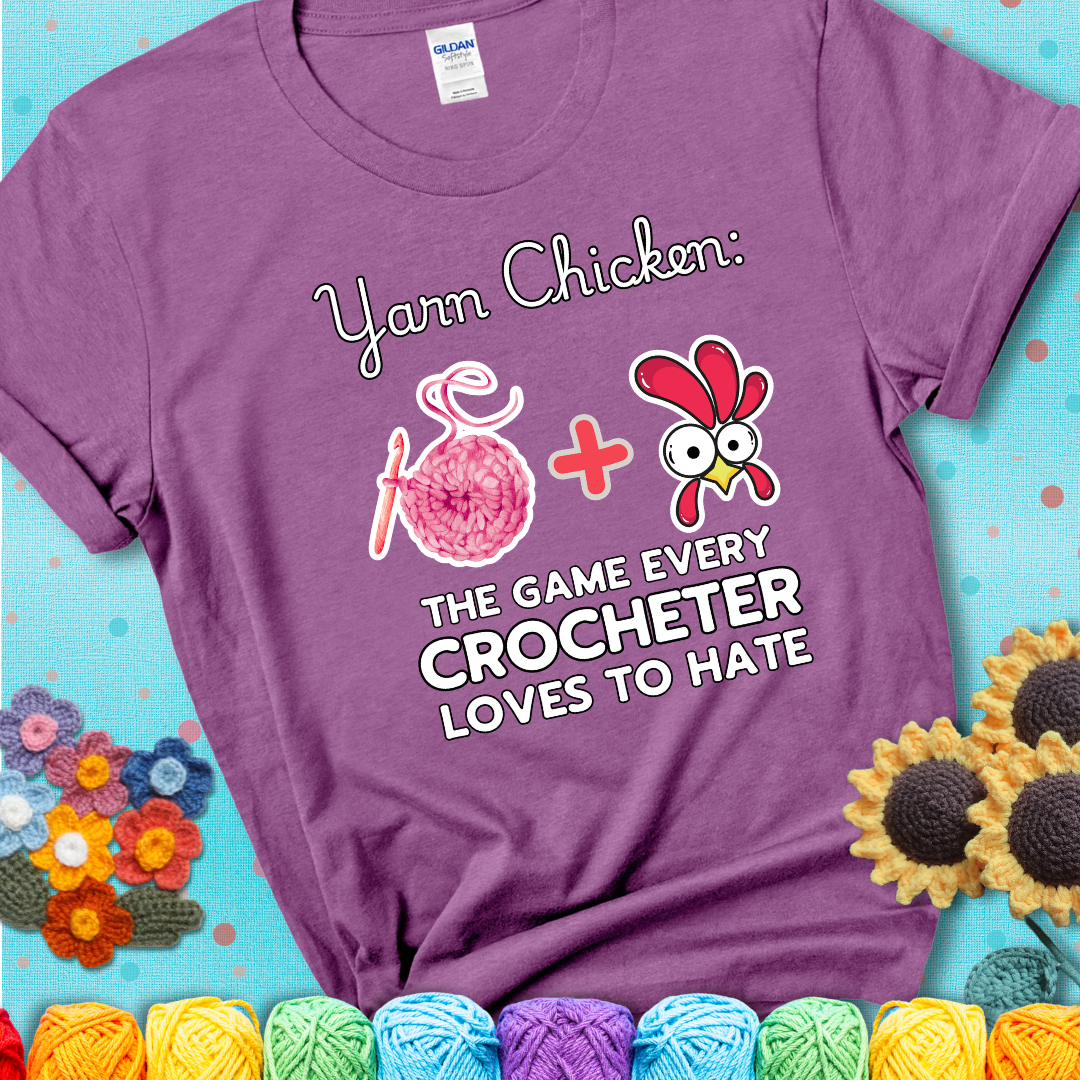 Cartoon chicken inside a yarn ball with crochet circle background. Text reads: “Yarn Chicken: The Game Every Crocheter Loves to Lose.” A fun and relatable tee for fiber artists who like to live on the edge, showing a lavender tee with a teal sunflower background