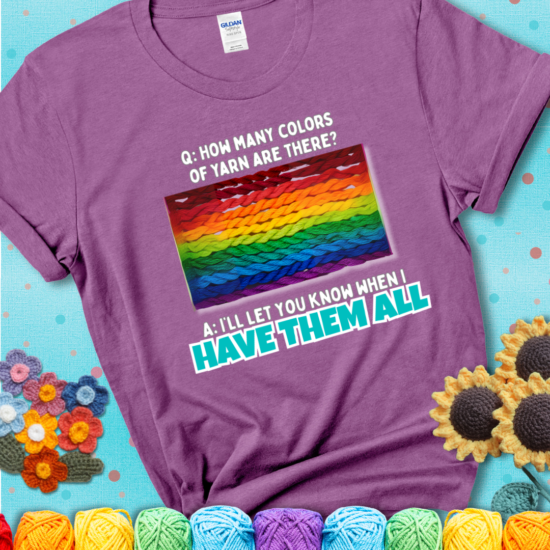 Light purple t-shirt with rainbow skeins of yarn stacked in color gradient with playful question: “How many colors of yarn are there?” Answer: “I'll let you know when I have them all.”