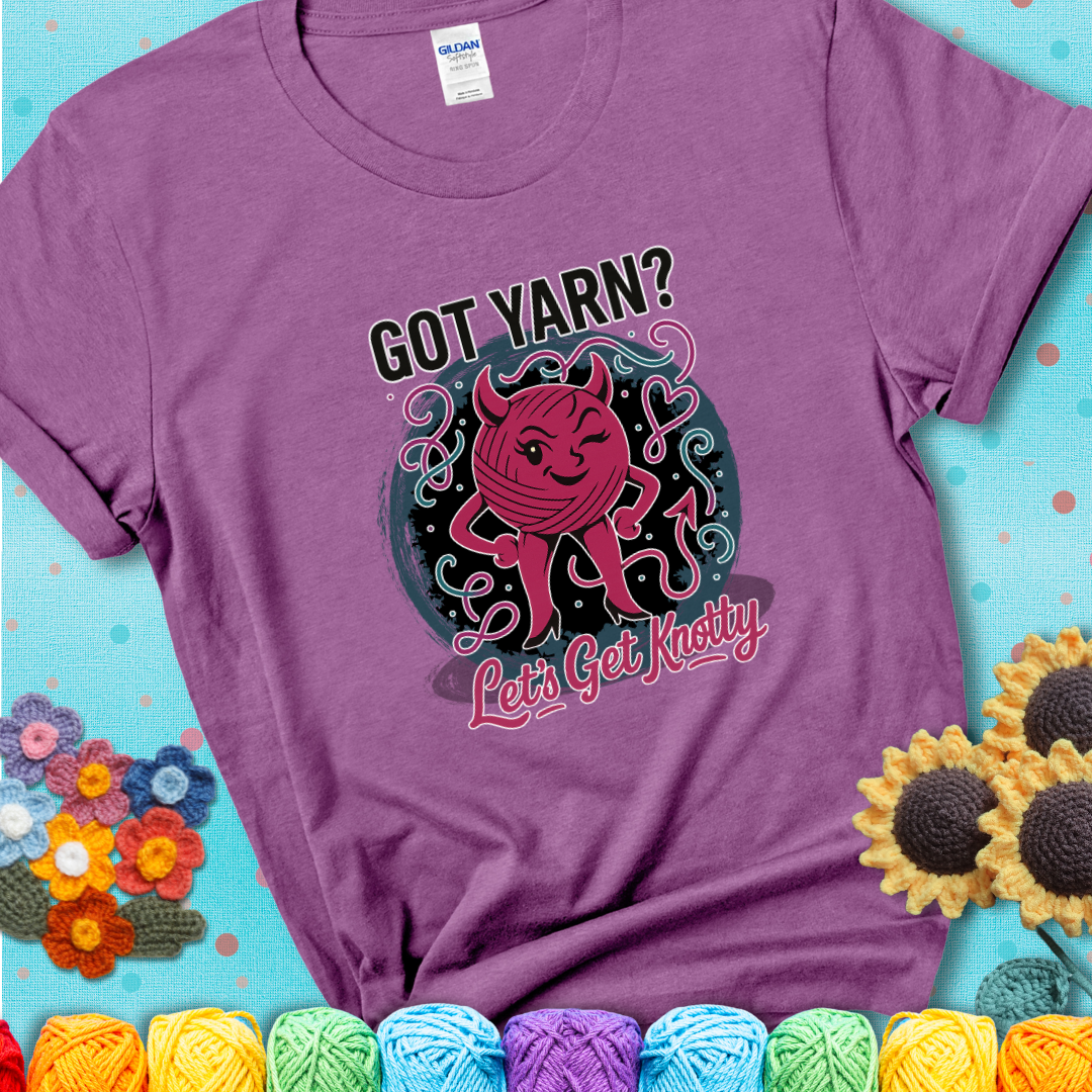 Heather Radiant Orchid t-shirt with a cheeky pink yarn ball wearing devil horns, arms, and legs, winking beneath the phrase “Got Yarn? Let’s Get Knotty