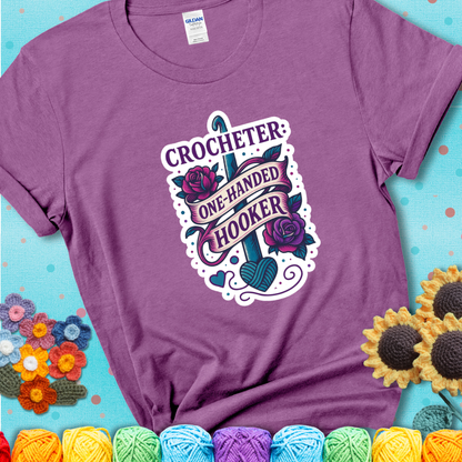 Heather Radiant Orchid t-shirt with a tattoo-style crochet design featuring a crochet hook, roses, and the phrase “Crocheter: One-Handed Hooker.”