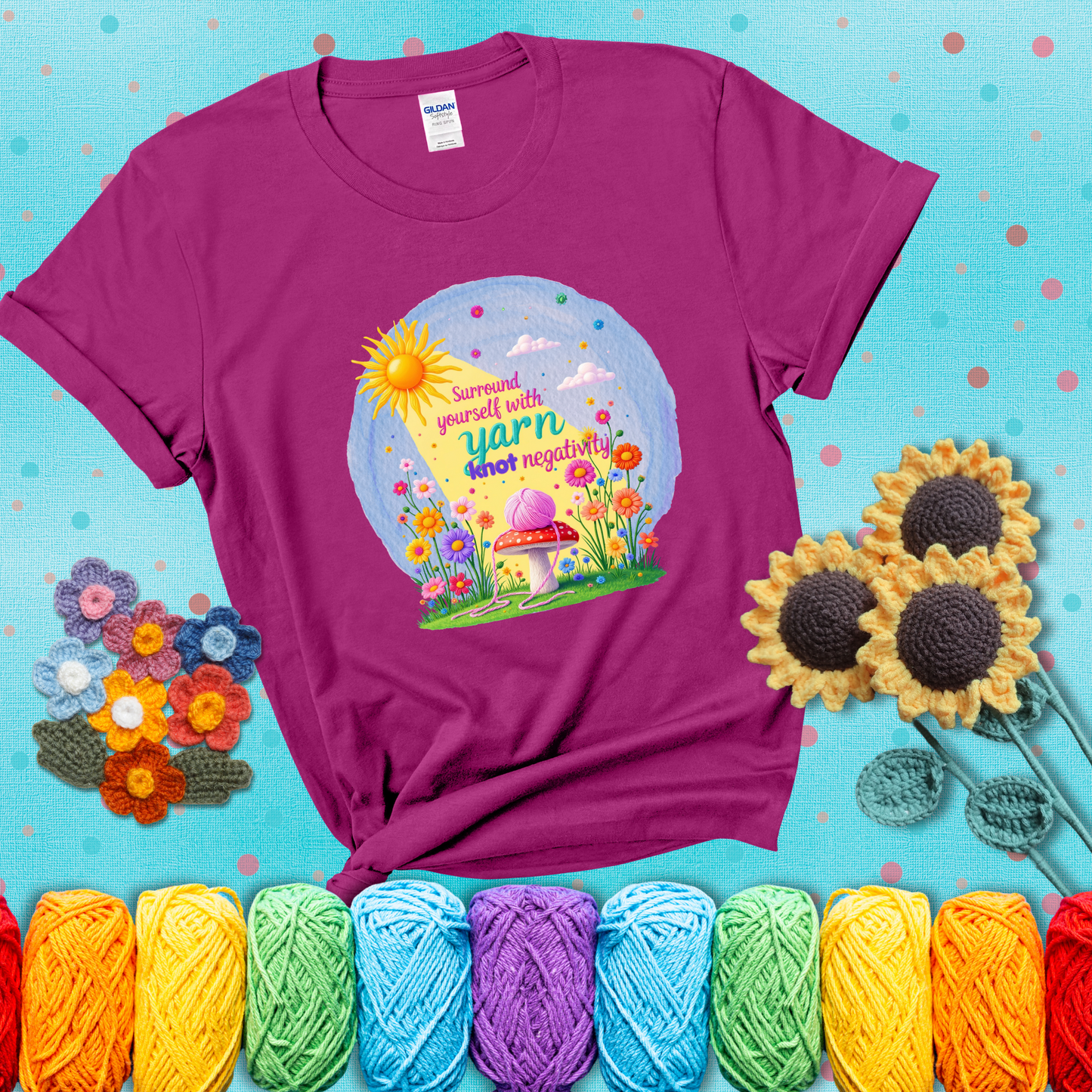 A happy spring garden scene with a sunbeam, flowers, and a pink yarn ball on a mushroom, with the quote "Surround yourself with yarn, knot negativity," showing a magenta tee with a teal sunflower background