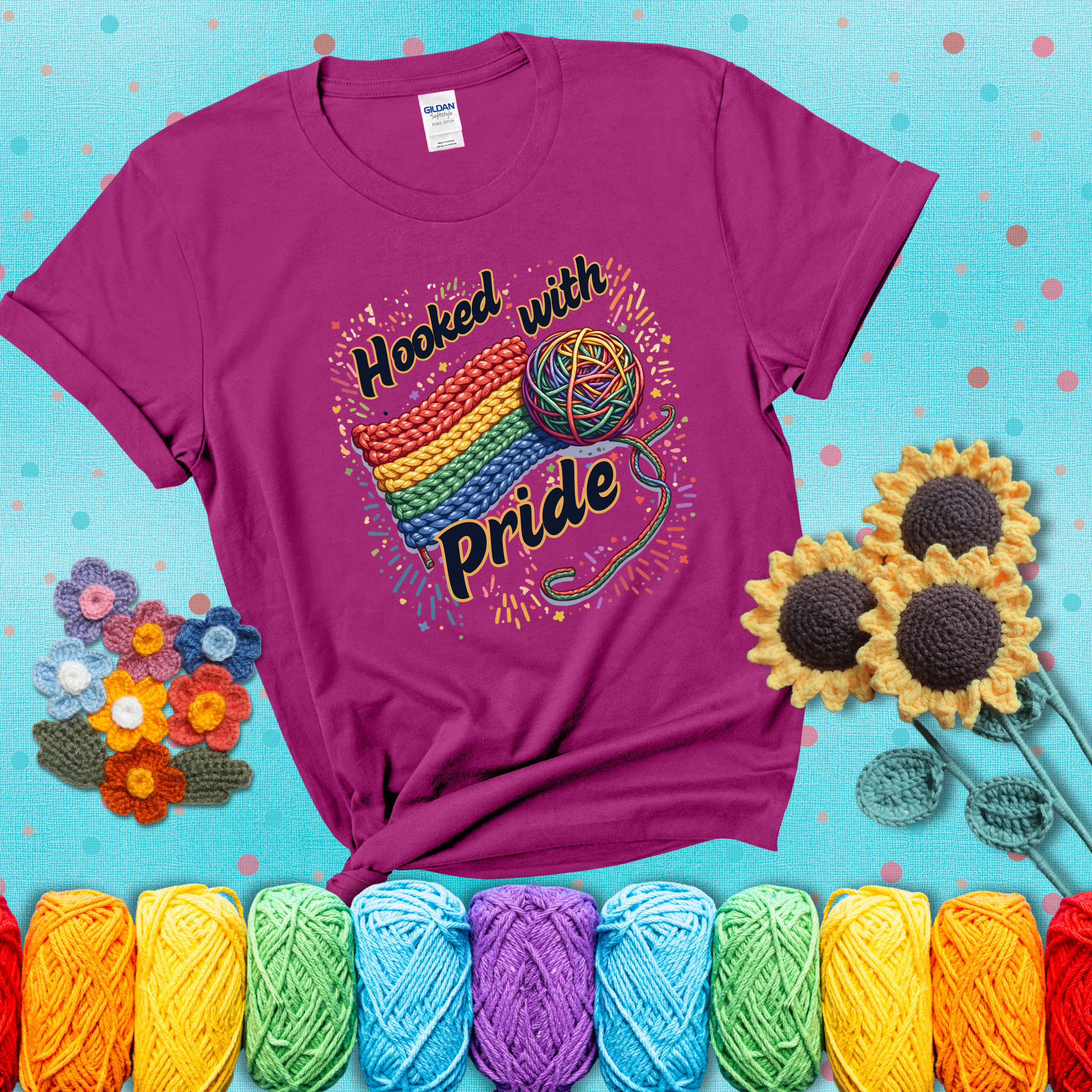 A rainbow-striped crochet swatch paired with a multicolor yarn ball and bold “Hooked With Pride” lettering. Confetti surrounds the vibrant scene showing a magenta tee with a teal sunflower background