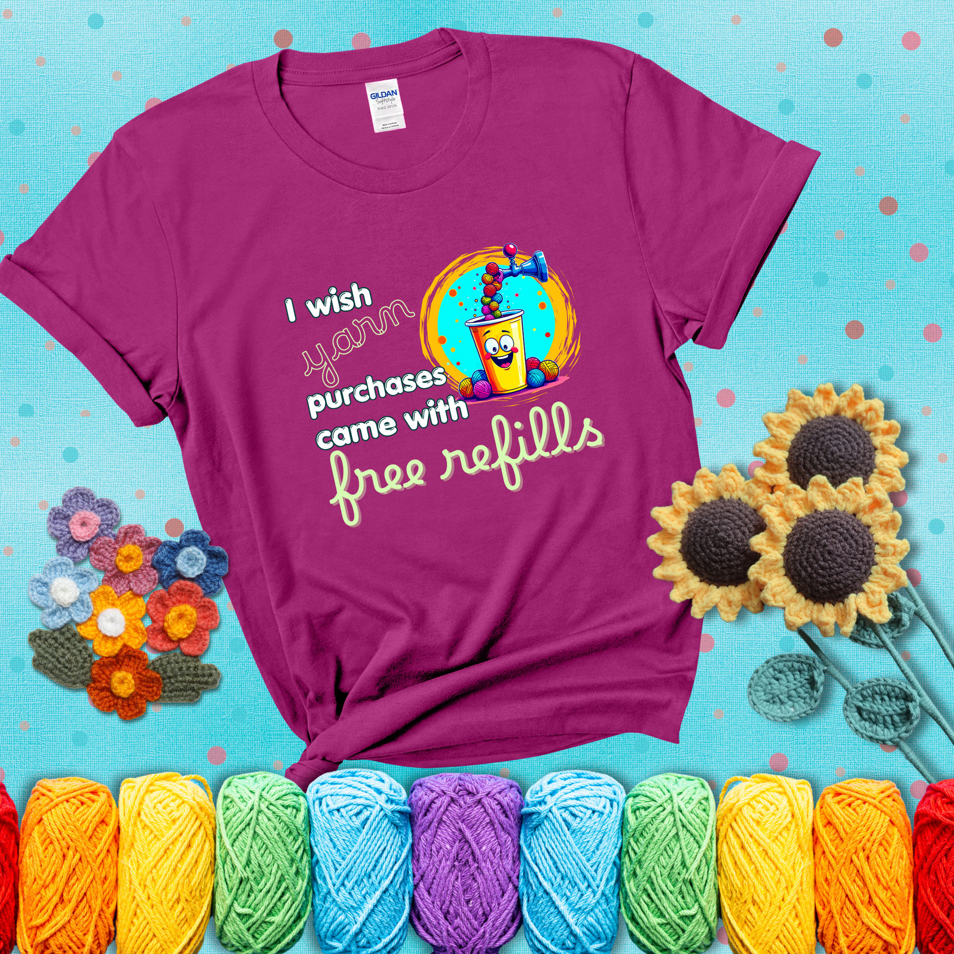 A bright yellow cup with a smiling face is being filled with colorful yarn balls from a soda machine, with the phrase “I wish yarn purchases came with free refills,” showing a magenta tee with a teal sunflower background