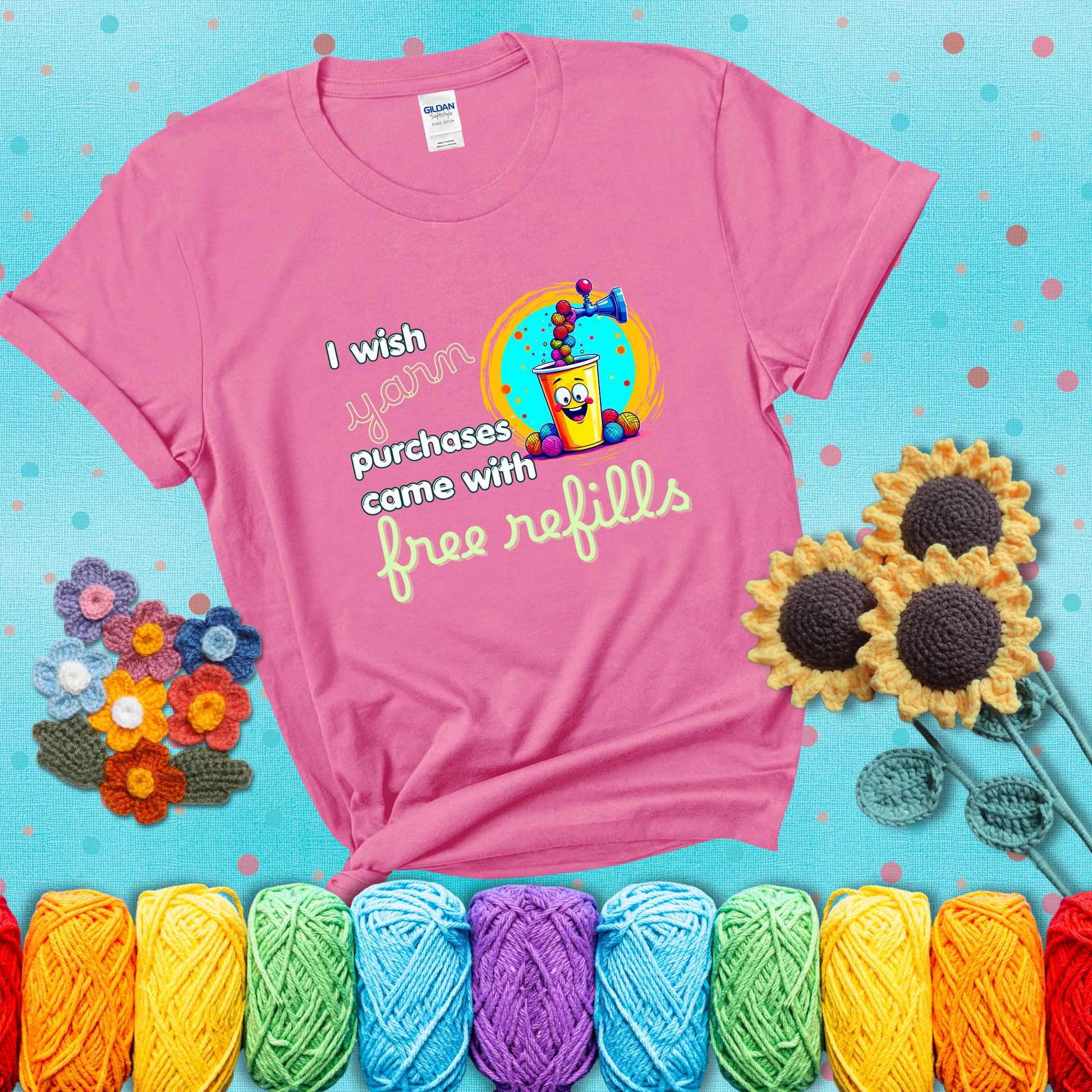 A bright yellow cup with a smiling face is being filled with colorful yarn balls from a soda machine, with the phrase “I wish yarn purchases came with free refills,” showing a pink tee with a teal sunflower background